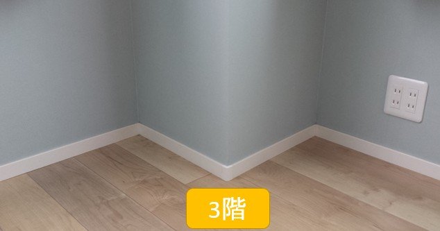 白いプラスティック巾木(木目フローリングと水色壁紙の間)